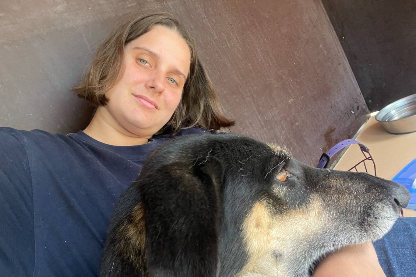 Ein Mensch mit kurzen Haaren liegt lächelnd neben einem Hund.